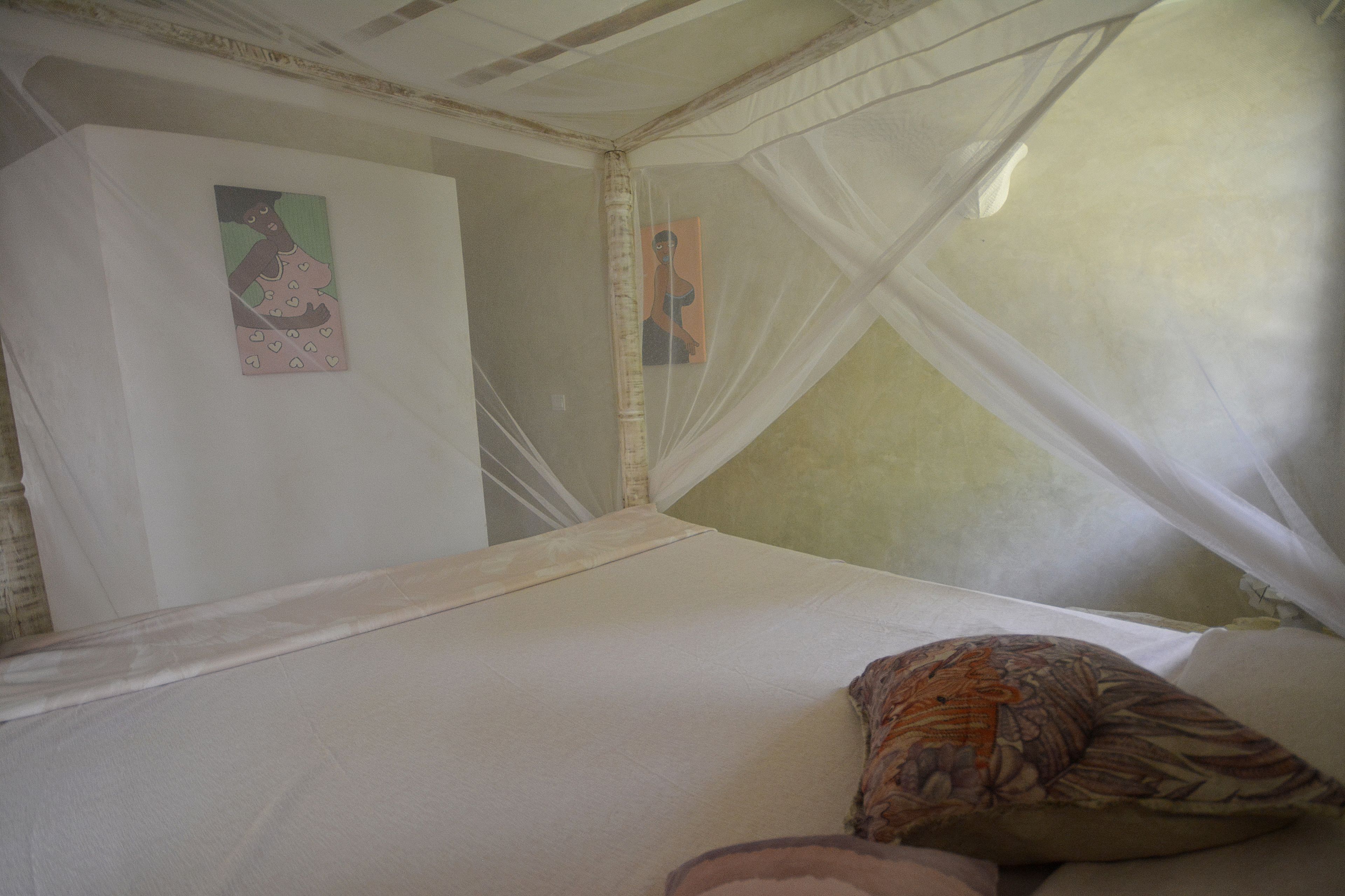 Une chambre avec un lit, une moustiquaire et deux tableaux accrochés aux murs.
