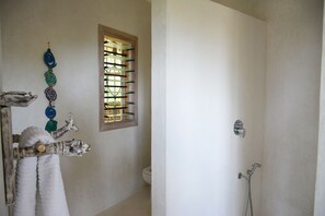 A bathroom with a shower, a toilet, and a window with blinds. - The Lawford Kenya (Malindi)