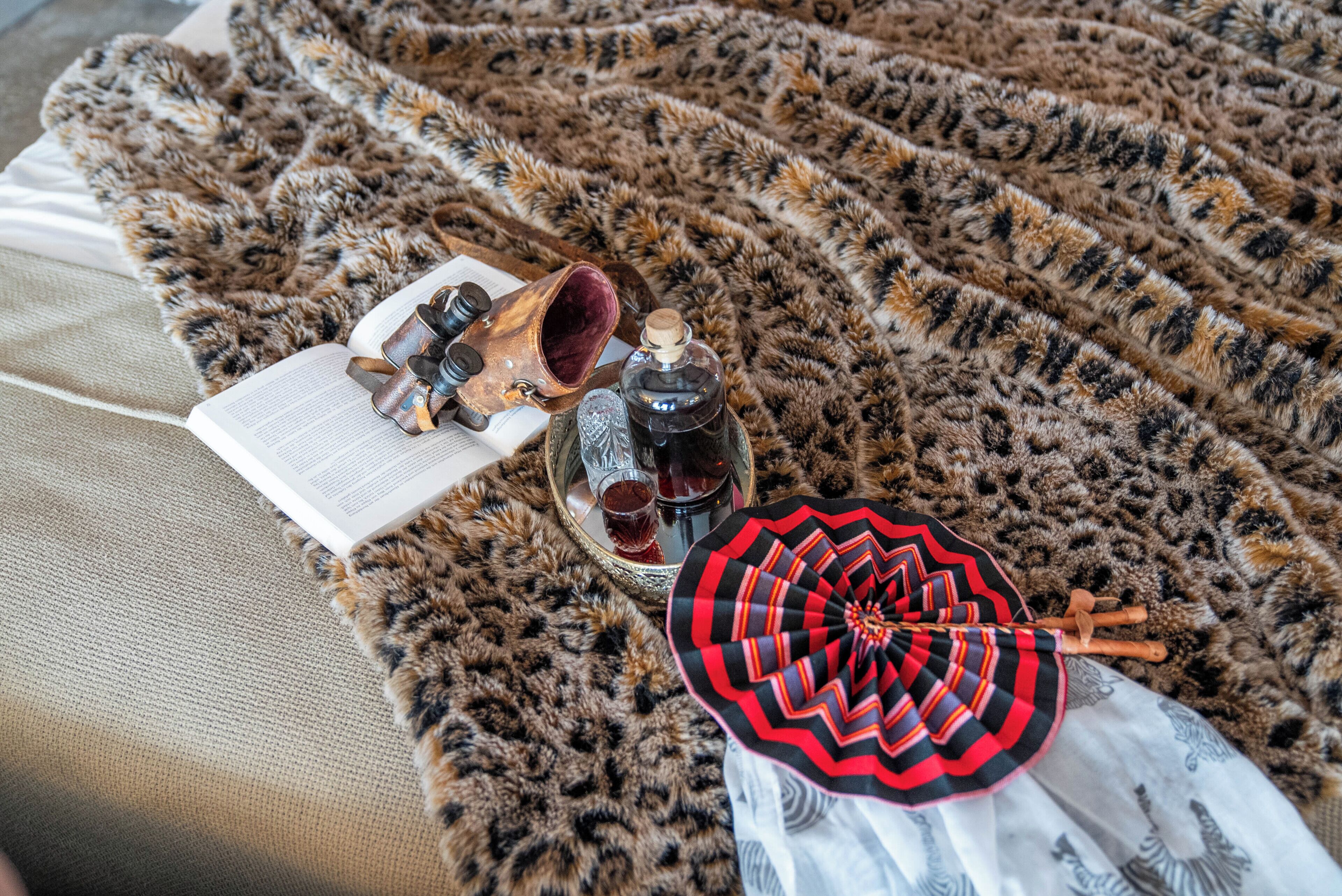 A leopard print blanket, a book, a pair of glasses, a bottle, and a patterned umbrella on a couch.
