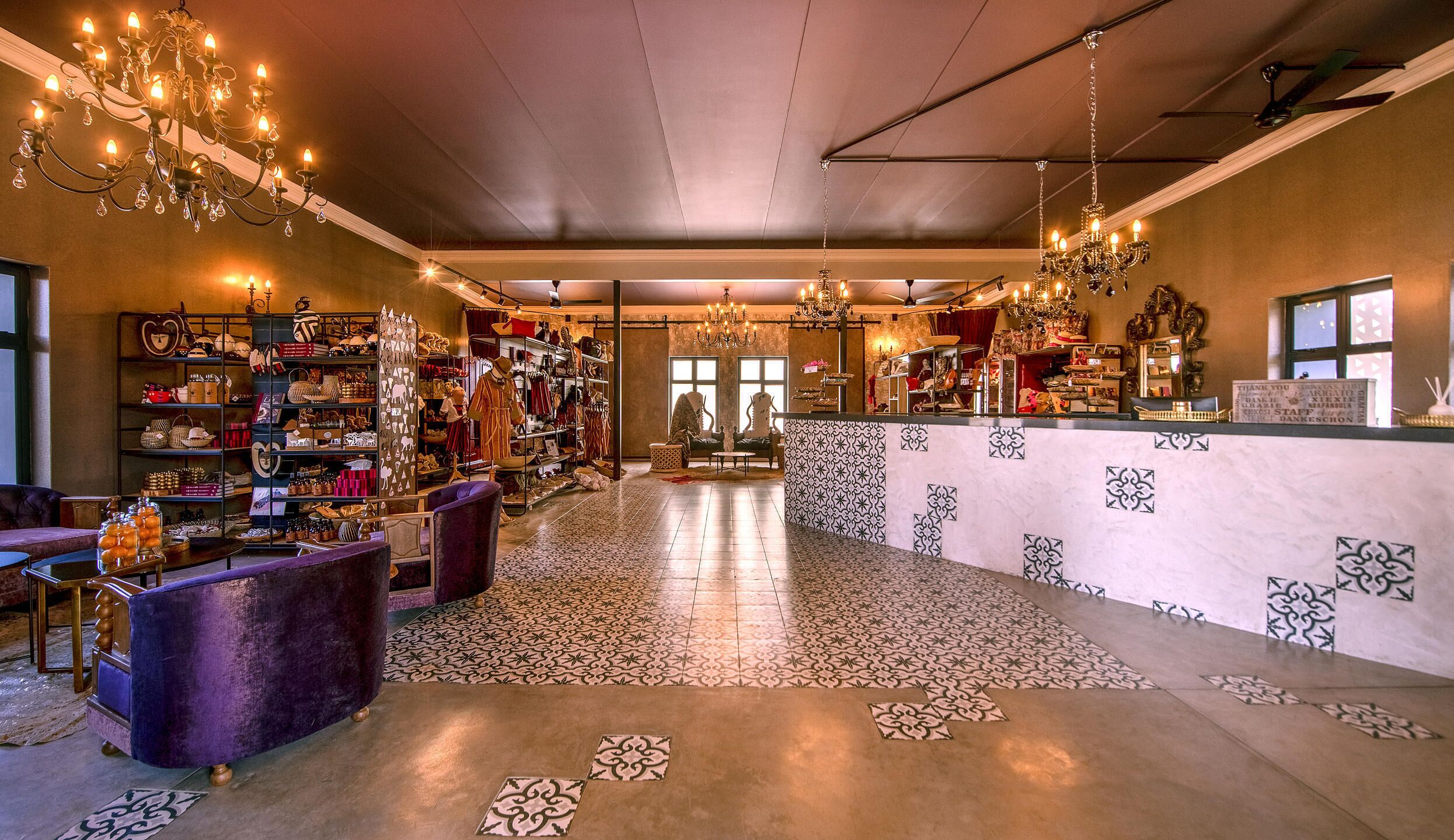A spacious boutique hotel lobby with a central seating area, a chandelier, and a variety of displayed items.