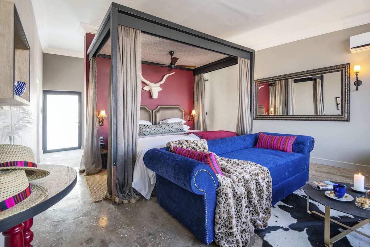 A bedroom with a four-poster bed, a blue sofa, a cow skull wall decoration, a mirror, and a small table with a candle.