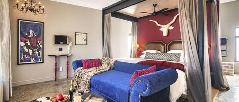 Un dormitorio con una cama grande, un sofá azul, una araña de techo y un tapiz de cuero de vaca.