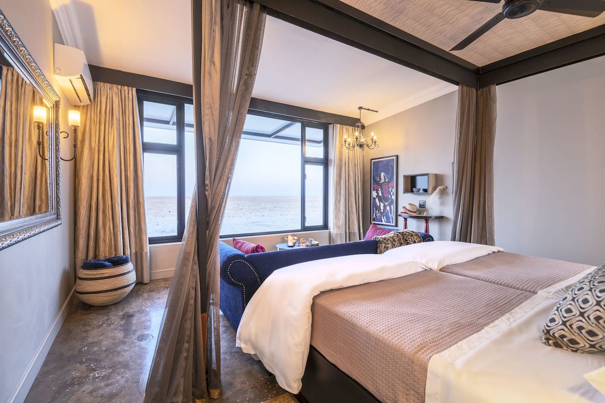A hotel room with a large bed, a seating area with a view of the sea, and a small table with a lamp.