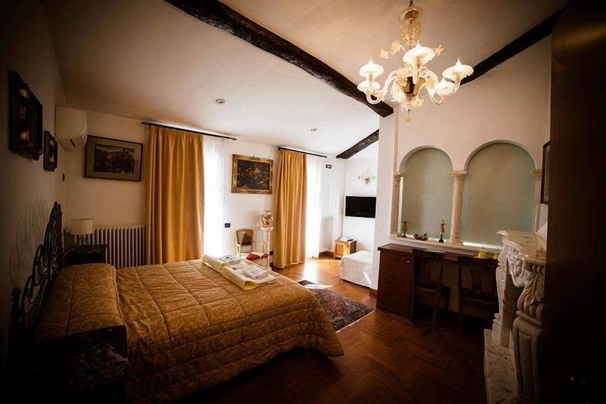A bedroom with a large bed, a desk, a chair, a mirror, and a chandelier.