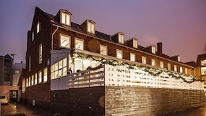 A brick building with multiple windows and a white fence decorated with greenery. - Hotel Sidesporet (Holbaek)