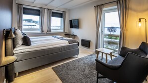 A modern hotel room with a large bed, a small table, a chair, a TV, and a balcony with a view. - Hotel Sidesporet (Holbaek)