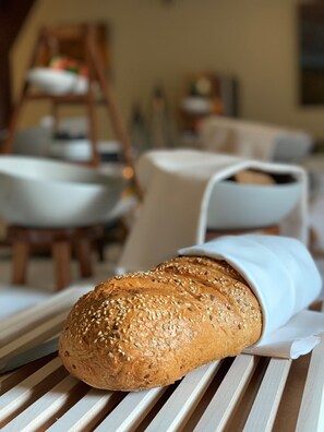 A loaf of bread on a wooden table with a white cloth, in a room with a wooden chair and a white tablecloth.