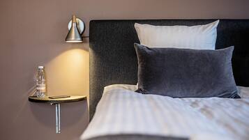 En pænt redt seng med to puder, et sengebord med en lampe, en vandflaske og en smartphone.