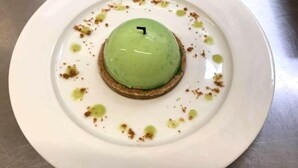 Postre a un plat blanc amb una cobertura verda, envoltat de molles marrons i salsa verda.