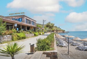 A coastal hotel with a patio area and beachside lounge chairs.