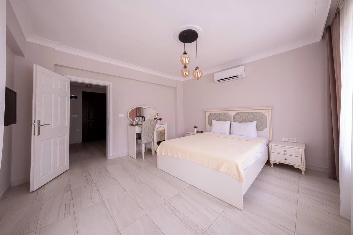 A bedroom with a bed, bedside tables, a vanity with a mirror, and an air conditioning unit.