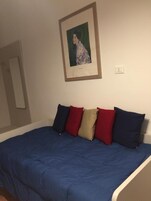 A bedroom with a bed, pillows, a framed picture on the wall, and a light switch.