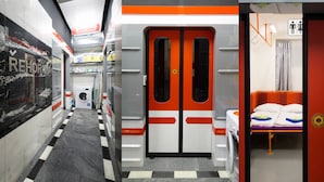 A train carriage with a checkered floor, a washing machine, and a bed with pillows and a blanket. - METRO Apartment (Prague)