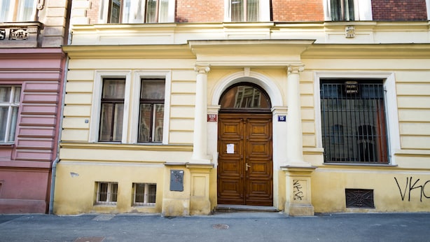 A building with a large wooden door, a small window with a metal grill, and a number '938' sign above the door. - METRO Apartment (Prague)