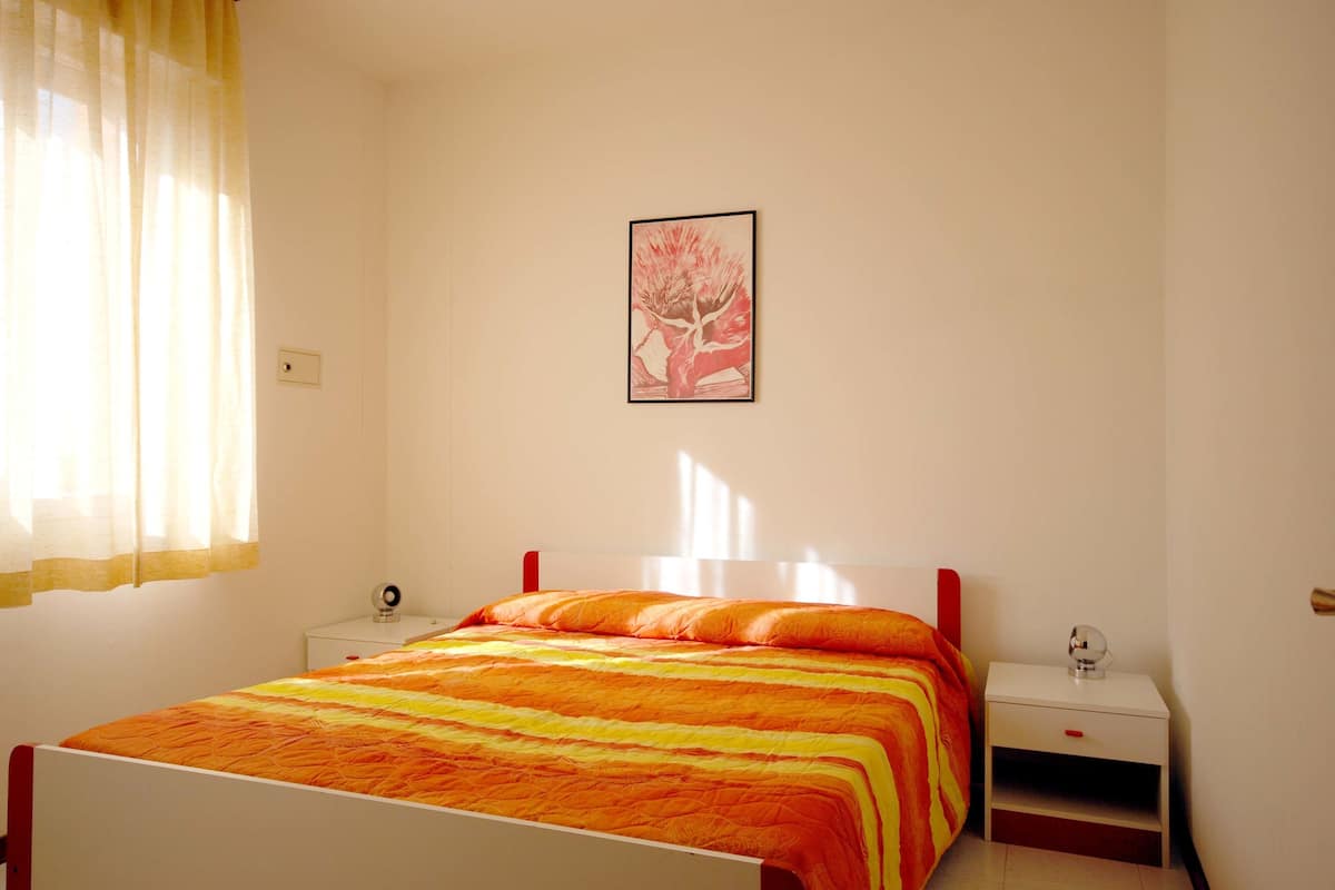 A bedroom with a bed, a nightstand, a lamp, and a framed picture on the wall.