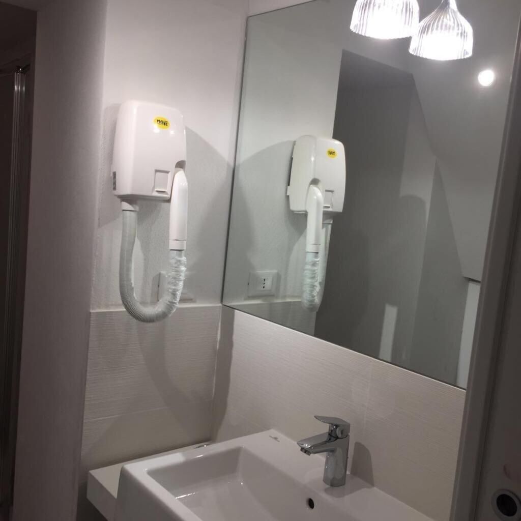 A bathroom with a white sink, a mirror, and two hair dryers mounted on the wall.
