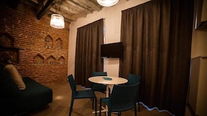 Una habitación acogedora con pared de ladrillo, una mesa redonda con sillas, un televisor de pantalla plana en la pared y un sofá.