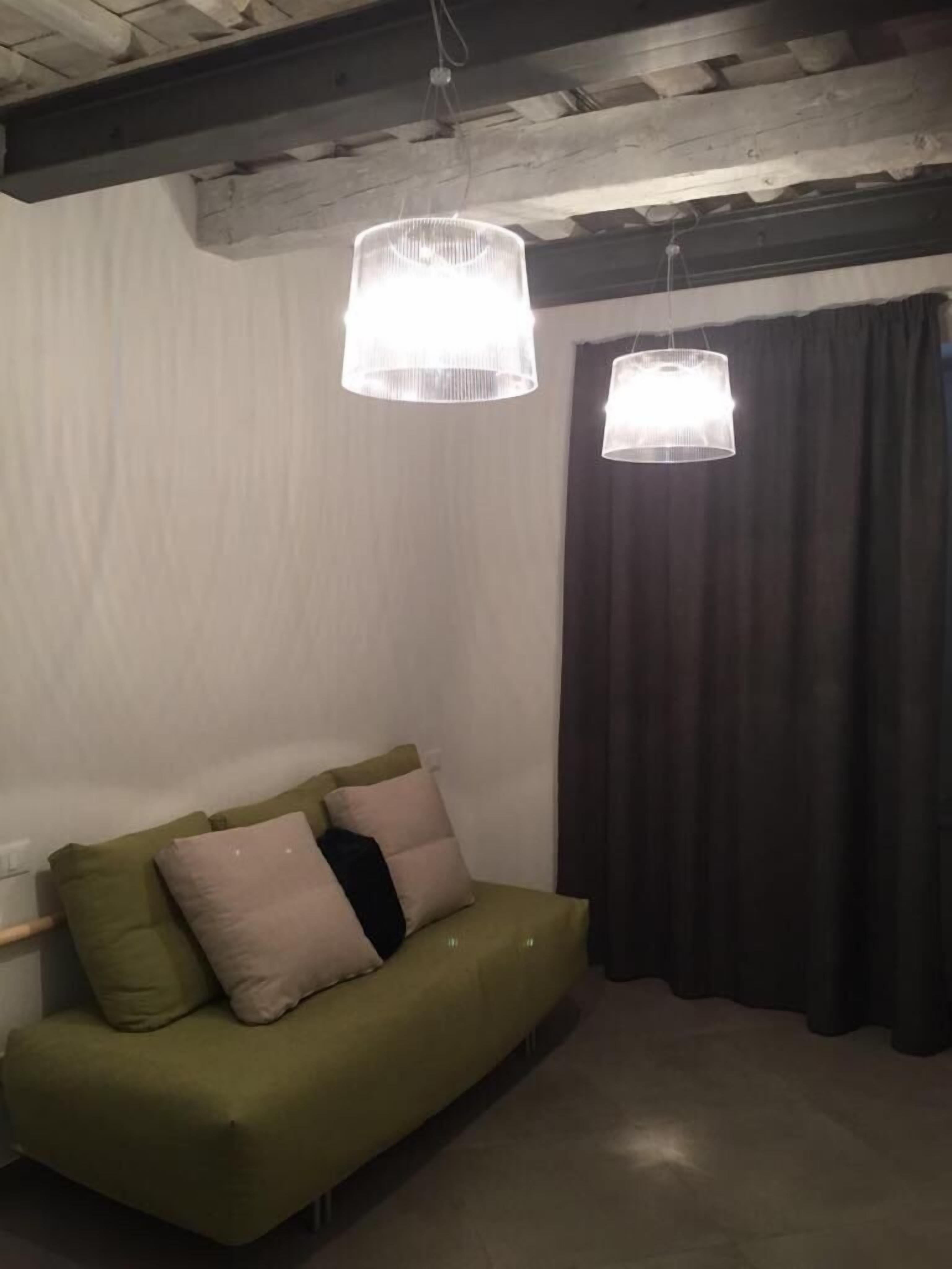 A green sofa with multiple cushions, two pendant lights, a dark curtain, and a wooden ceiling beam.