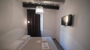 Habitación de hotel con cama, televisor de pantalla plana en la pared y lámpara colgante.