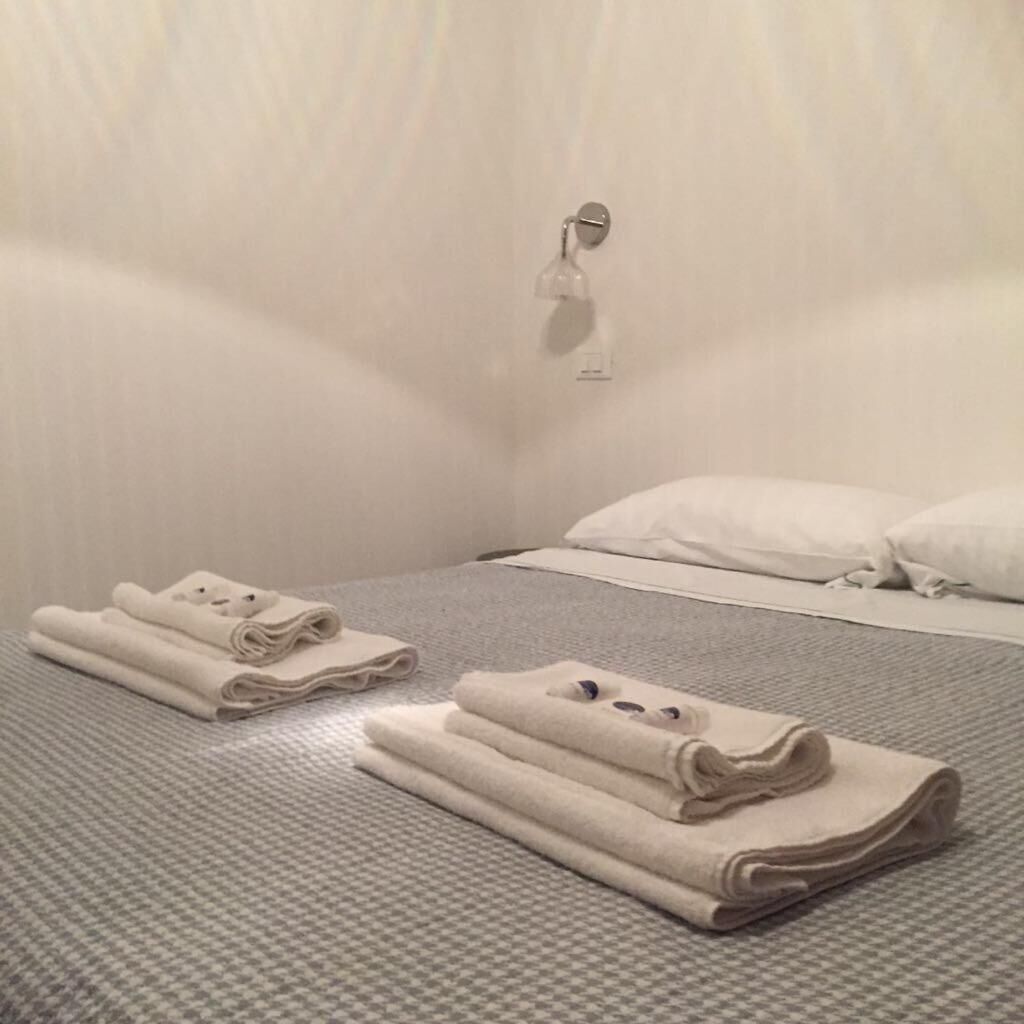 Une chambre d’hôtel avec un lit bien fait, un luminaire fixé au mur et un sol à carreaux.