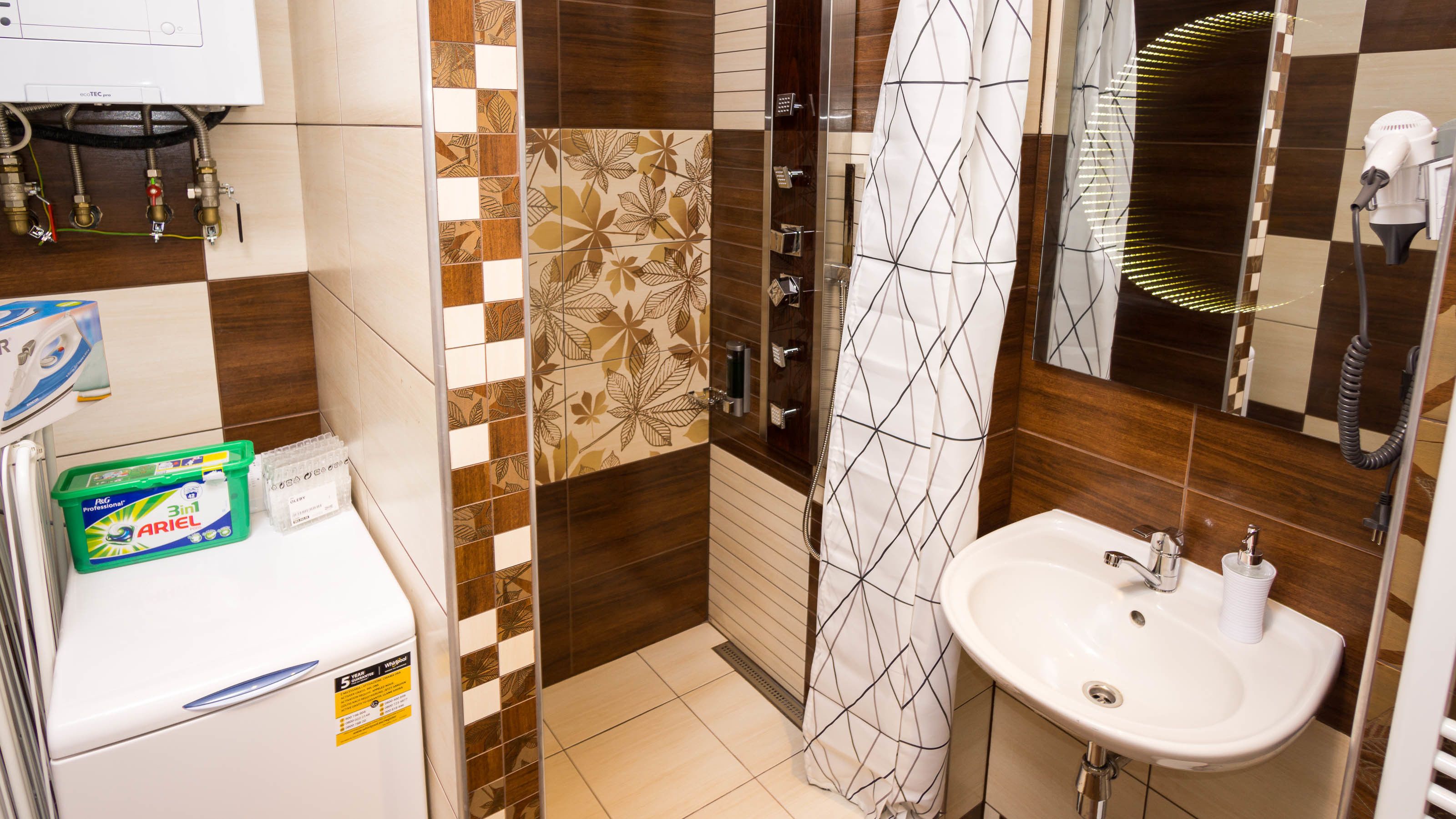 Un baño con un lavamanos blanco, un espejo, una ducha con cortina de estampado geométrico y un inodoro.