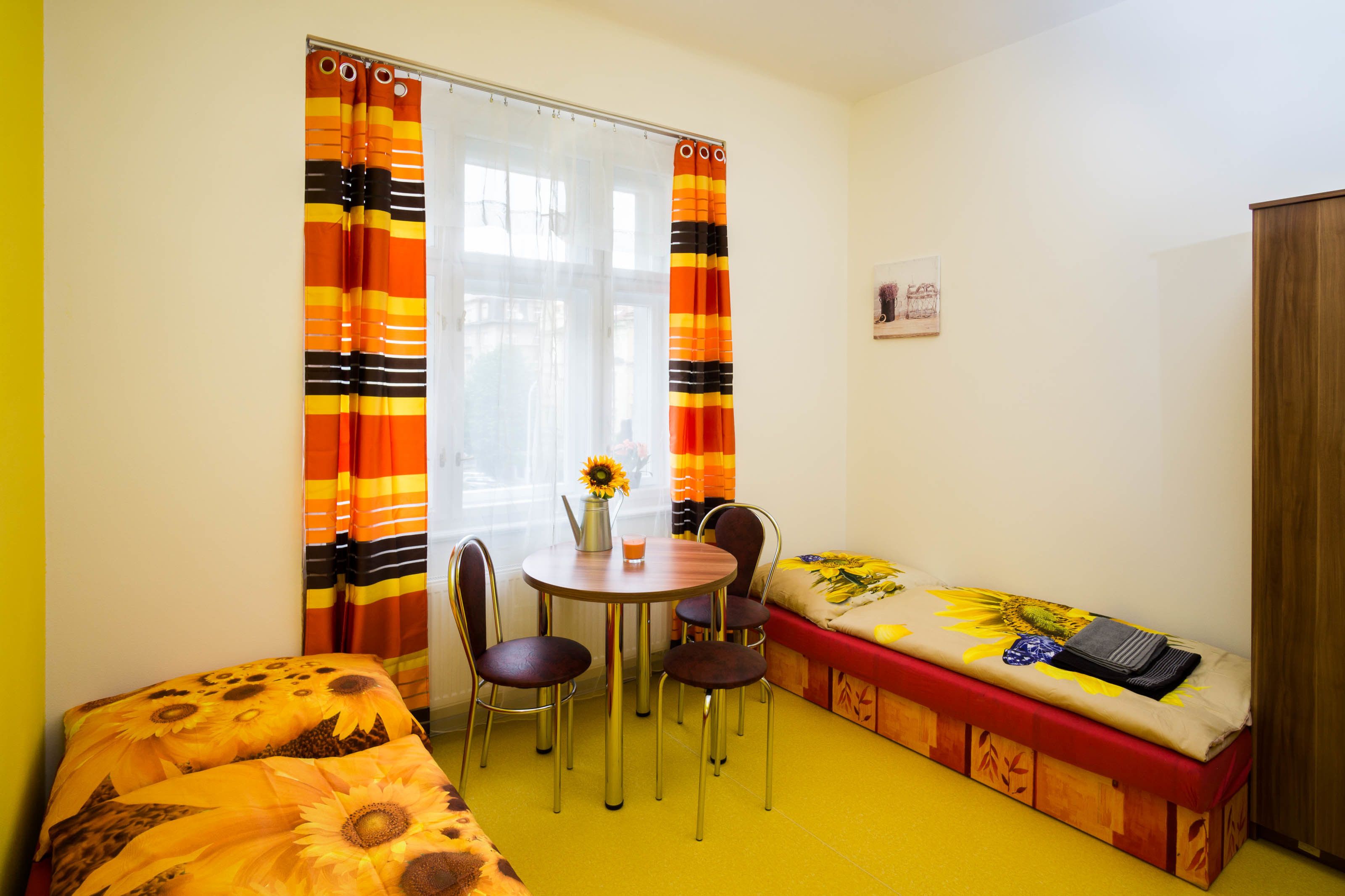 Een kleine kamer met een bed, een tafel met stoelen en een raam met gordijnen.