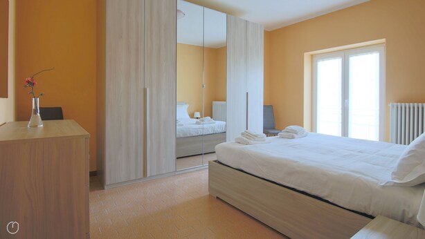 A hotel room with a bed, a desk, a chair, a mirror, a window, and a radiator. - Italianway - Casasco 79 (Centro Valle Intelvi)