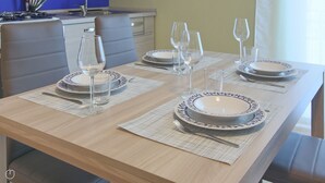 A dining table set with plates, glasses, and cutlery, with a kitchen in the background. - Italianway - Casasco 79 (Centro Valle Intelvi)