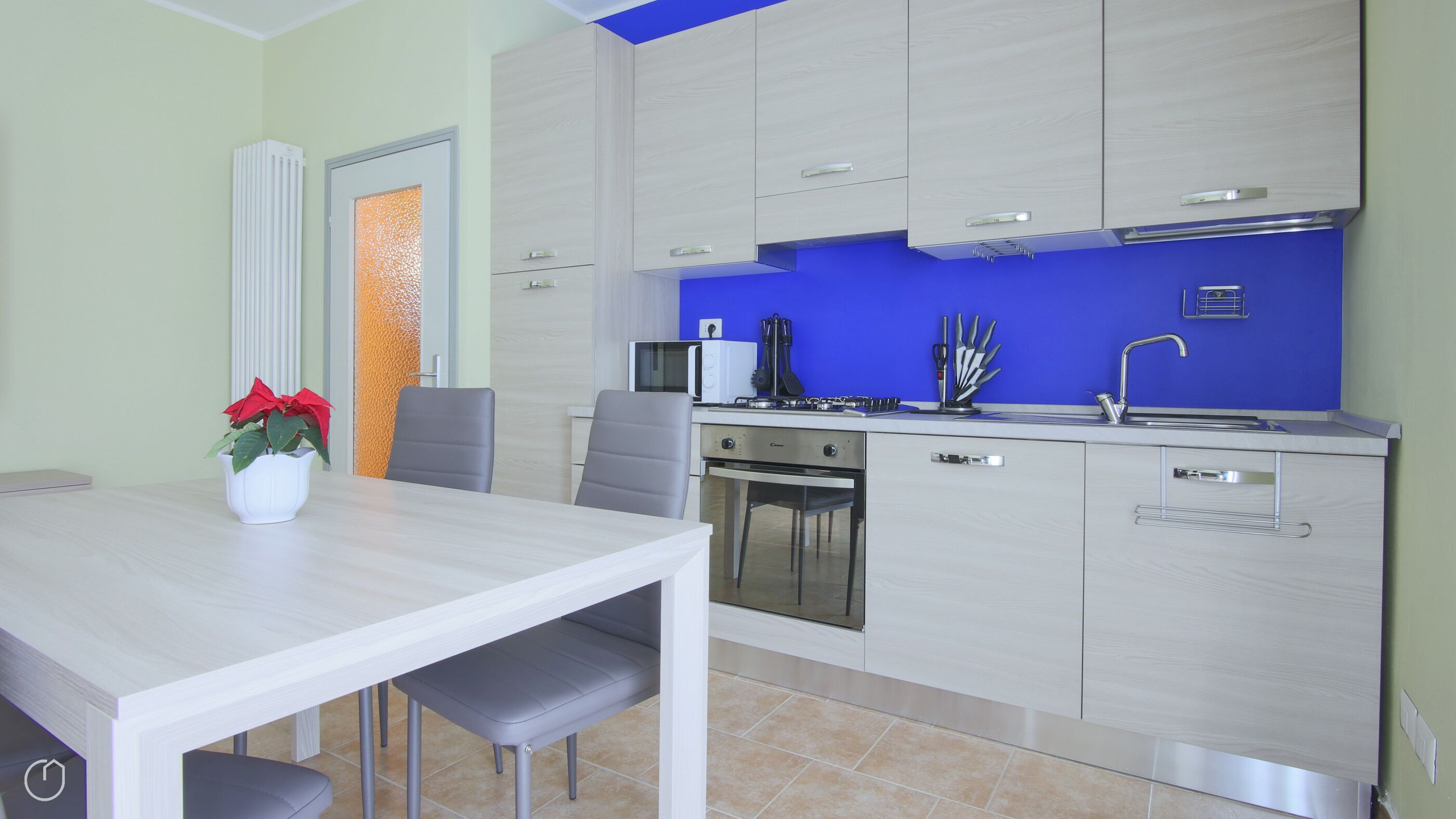 A modern kitchen with a blue backsplash, stainless steel appliances, and a dining area with a white table and chairs.