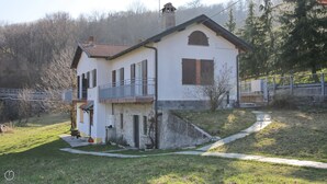 A two-story house with a balcony, a chimney, and a small garden area. - Italianway - Casasco 79 (Centro Valle Intelvi)