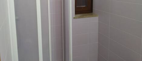 A bathroom with a shower enclosure, a sink, and a window.