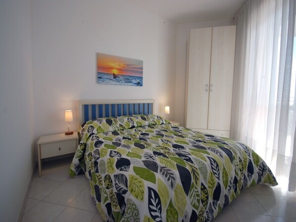 A bedroom with a bed, a nightstand, a wardrobe, and a painting of a sunset over the ocean. - Residence Bianco e Nero (Lignano Sabbiadoro)