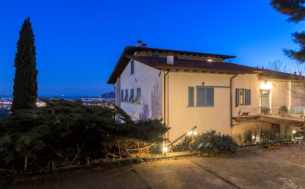 A two-story house with a balcony, a garden, and a view of the city at dusk. - Ca' Bianca Bed & Breakfast (Fosdinovo)