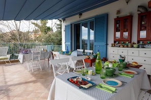 An outdoor dining area with tables set for a meal, a kitchen with cabinets, and a view of the surrounding area. - Ca' Bianca Bed & Breakfast (Fosdinovo)