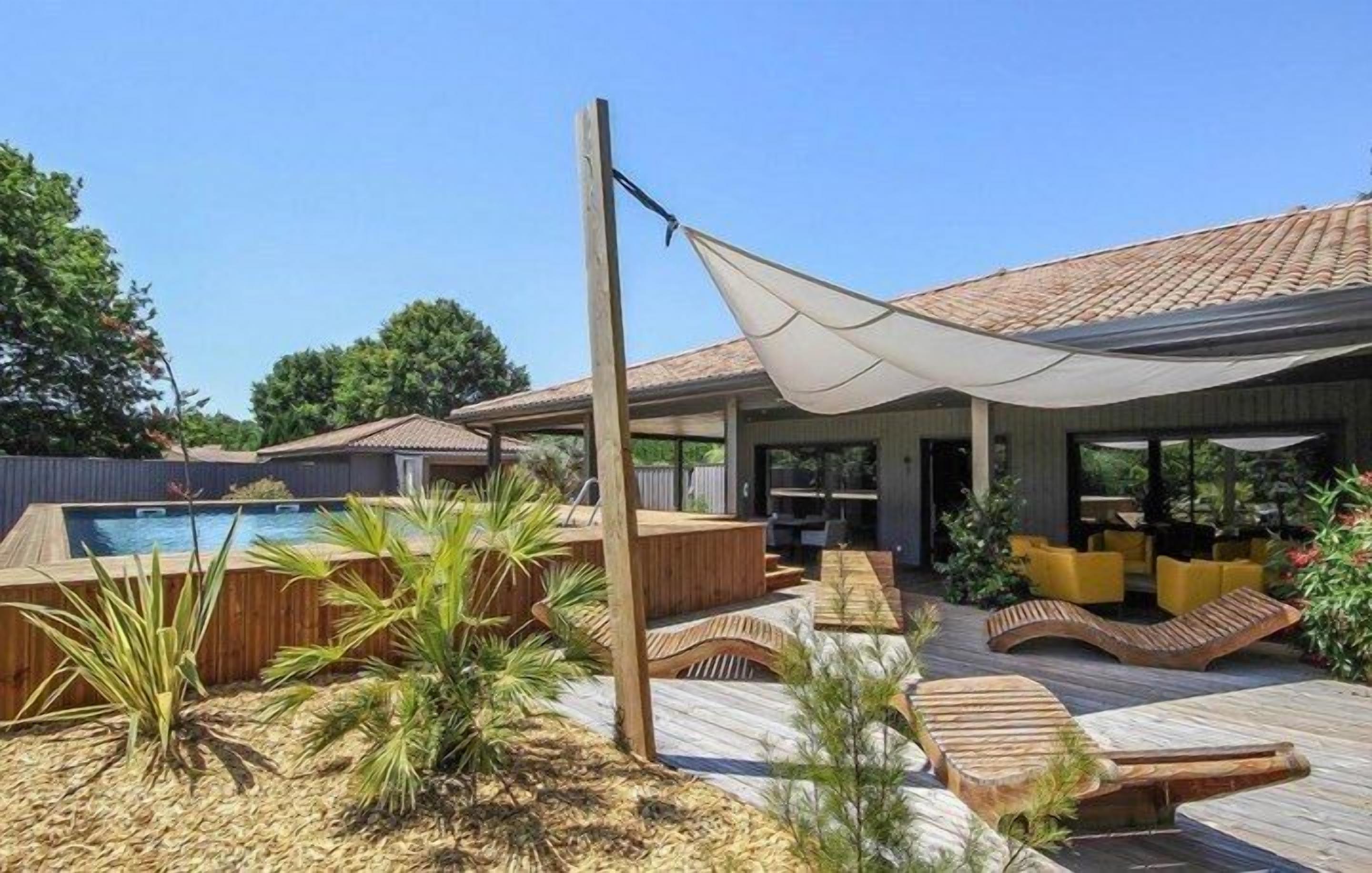 A poolside area with a hot tub, wooden deck, lounge chairs, and a covered seating area.