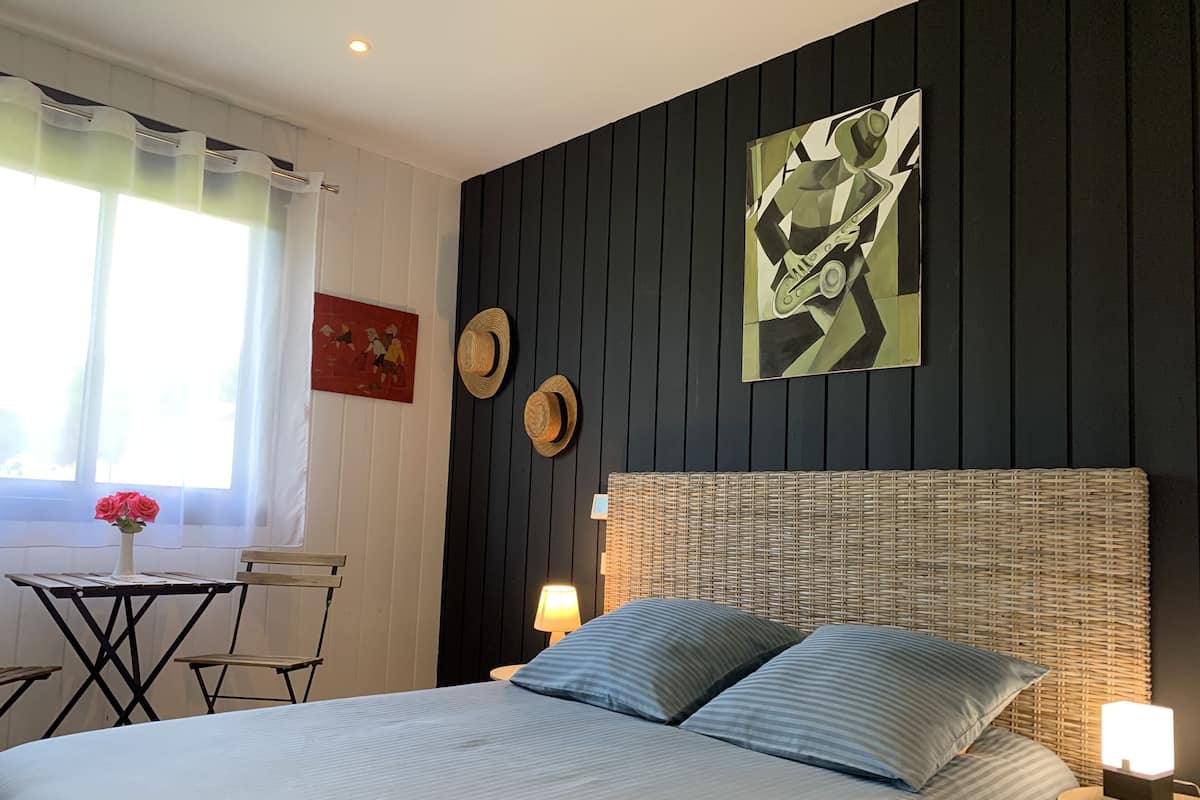 Une chambre à coucher avec un lit, un bureau, deux chaises, une lampe et un tableau au mur.
