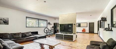 Een moderne woonkamer met een hoekbank, een salontafel, een televisie en een fiets op de achtergrond.