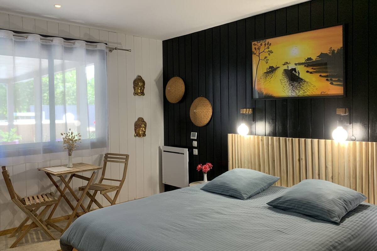 Une chambre à coucher avec un lit, un bureau et des chaises. Il y a un tableau au mur et une fenêtre avec des rideaux.