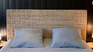 A bed with a woven headboard, two pillows, and a painting of a beach scene above it. - Villa Maya Uma (Vendays-Montalivet)