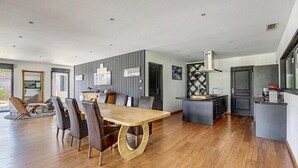 A modern kitchen with a central island, a dining area with a large wooden table, and a living space with a sofa and chairs. - Villa Maya Uma (Vendays-Montalivet)