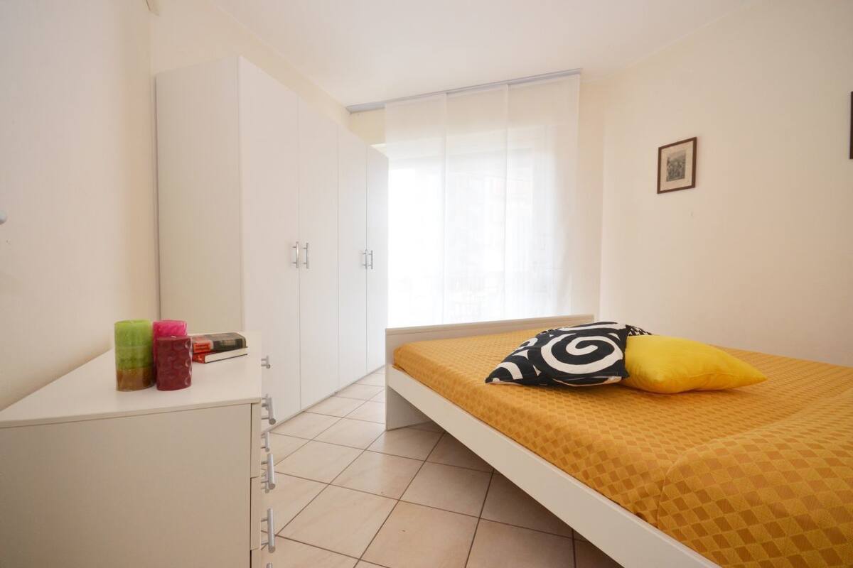 Ein Schlafzimmer mit Bett, Kleiderschrank, einem Fenster mit Vorhängen und einem kleinen Bild an der Wand.