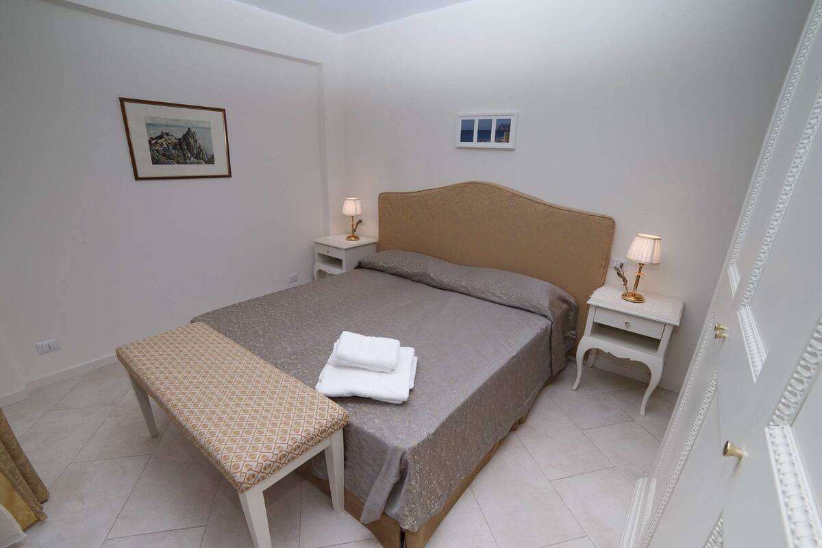 A neatly arranged hotel room with a bed, bedside tables, a bench, and a framed picture on the wall.