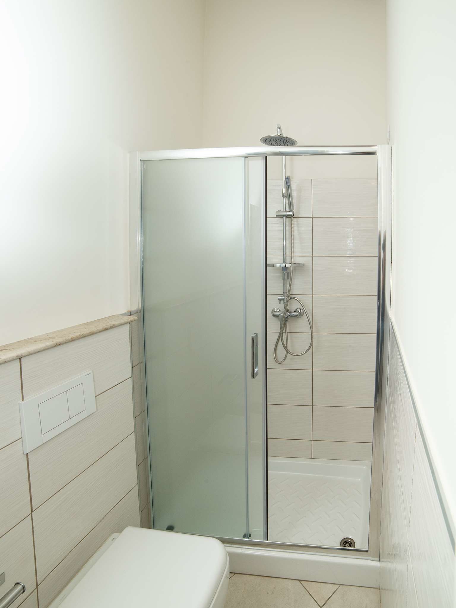 A small, enclosed shower area with a glass door, tiled walls, and a white toilet.