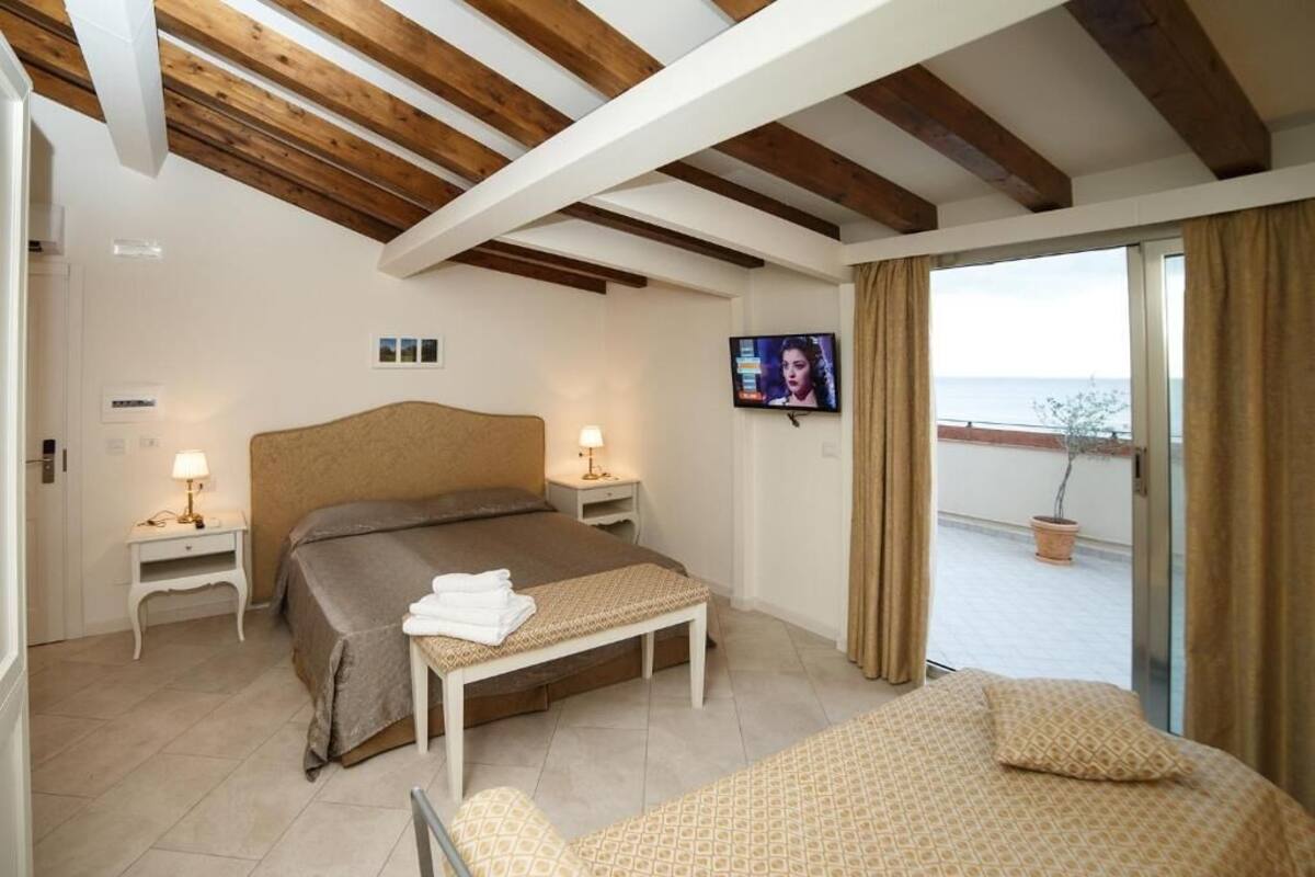 A bedroom with a bed, bedside tables, a TV, and a balcony with a view.
