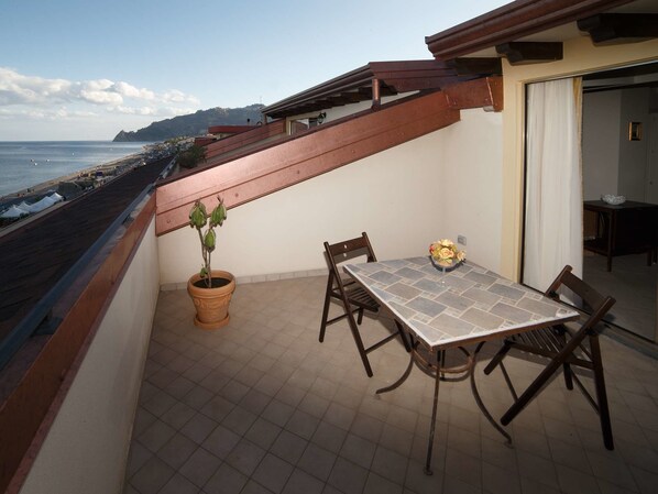 A balcony with a table and chairs, a potted plant, and a view of the beach and ocean. - Marina Di Savoca (Santa Teresa di Riva)