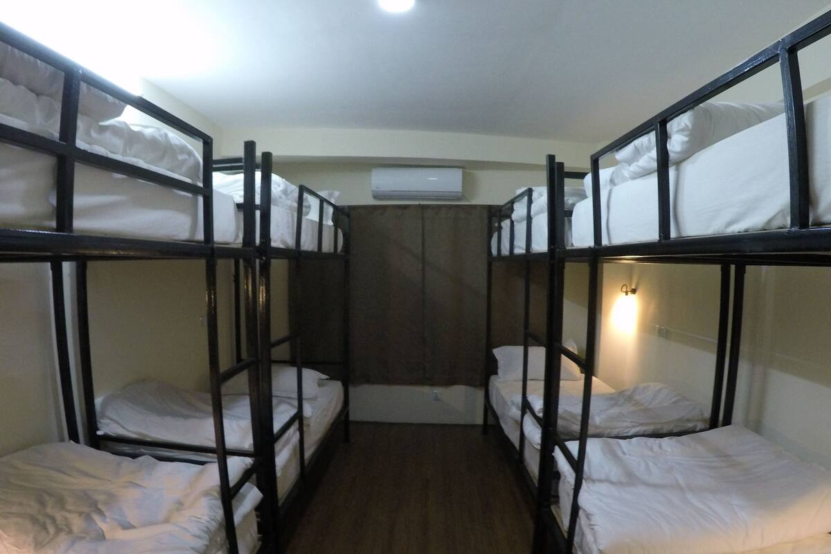Una habitación con literas, suelo de madera y aire acondicionado de pared.