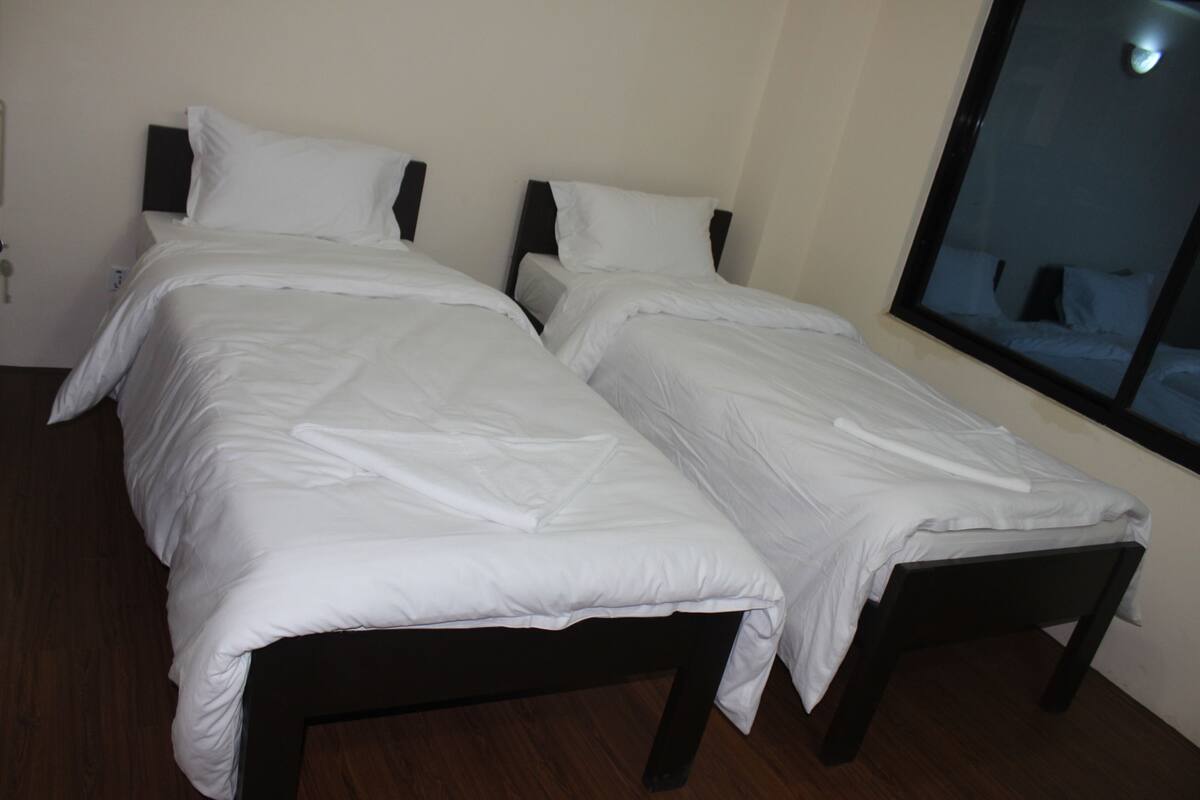 Habitación de hotel con dos camas individuales, cabeceros de madera, ropa de cama blanca y un ventanal grande.