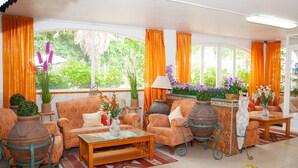 Un salón amplio con sofás de estampado naranja, una mesa de centro de cristal y macetas decorativas grandes.