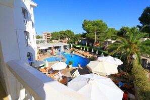 A pool area with umbrellas, lounge chairs, and a view of the surrounding buildings. - Atalaya Bosque Apartamentos (Calvia)