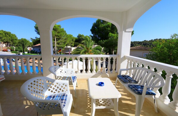 A covered outdoor seating area with white furniture and a view of the surrounding landscape. - Atalaya Bosque Apartamentos (Calvia)
